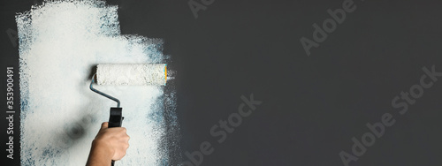 Professional decorator painting grey wall with white dye, space for text. Banner design photo