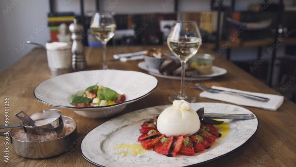 Burrata with tomato and basil. A beautiful dish and a glass of wine are standing on the table at the restaurant. Burrata dish served by the restaurant. Beautiful composition with a dish of wine. Burrata with tomato and basil. A beautiful dish and a glass of wine are standing on the table at the restaurant. Burrata dish served by the restaurant. Beautiful composition with a dish of wine.