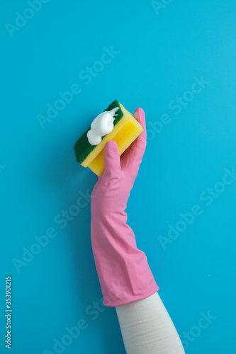 Women hand wearing glove holding sponge with soap for cleaning on blue background