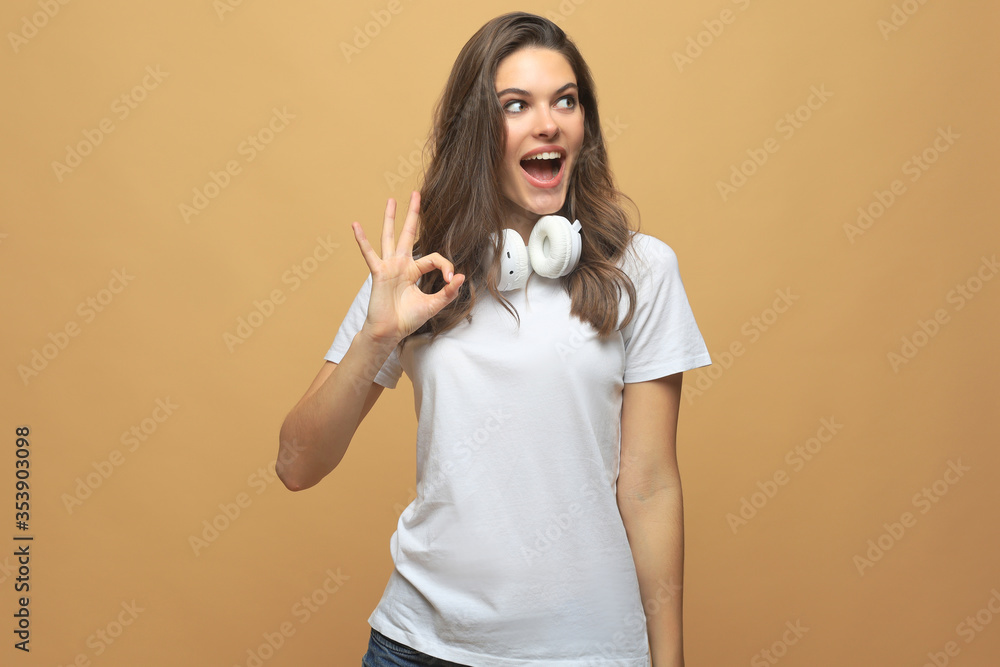 Portrait of young cheerful smiling woman showing okay gesture, with copyspace over beige background. Portrait of young cheerful smiling woman showing okay gesture, with copyspace over beige background.