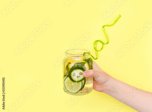 fruit lemonade in hand. Summer fruit drink in a glass jar with lime, lemon and mint on a yellow background. Cold alcoholic mojito. relaxation, party and good mood. Copy space.