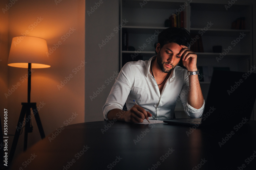 Young man working on computer at night in dark office. Business man working late at night from home / office Young man working on computer at night in dark office. Business man working late at night from home / office