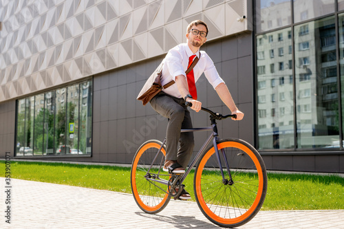 Elegant man in formalwear and eyeglasses looking forwards while going by bicycle