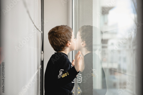 Dziecko, mały chłopiec wyglądający przez szybę, okno 
