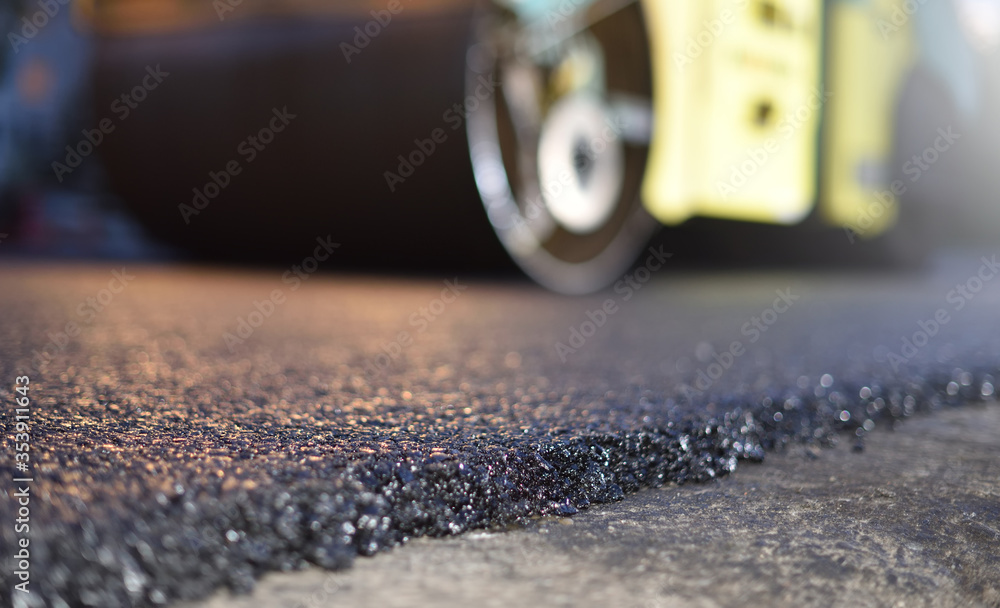 Road repair, thin layer of new asphalt close-up and road roller Road repair, thin layer of new asphalt close-up and road roller