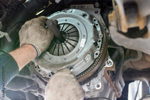 Car repair in a car service. Replacing the clutch disc of a gearbox on a car at a service station. Hands of a professional car mechanic. Cars repair technology. Technical photography. photo