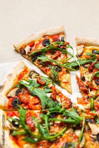 Colorful vagetarian pizza on crusty dough baked in Italian restaurant.Traditional fast food meal cooked with recipe from Italy delivered in box.Arugula leaves,dry tomatoes,white mushrooms,black olives photo