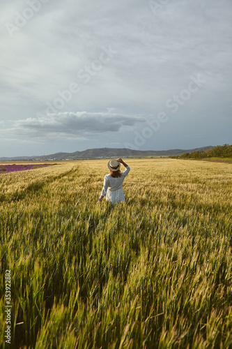 Here and Now. Young woman in hat posing in a cultivated wheat field on a summer day