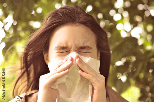 Young girl is blowing her nose near spring tree in bloom. Health and medicine concept