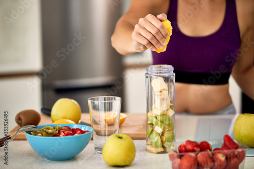 Close-up of sportswoman using lemon while making fruit smoothie at home.