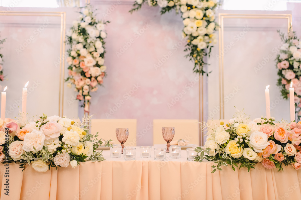 Fototapeta premium Banquet, restaurant. Table setting. On the table is a pink tablecloth. Presidium, table of the newlyweds. There is a tablecloth on the table. Floral arrangements in peach pink hues. Tall candles