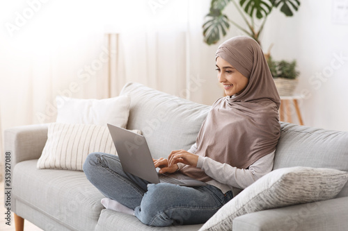 Modern Freelance. Smiling Muslim girl in hijab working on laptop at home