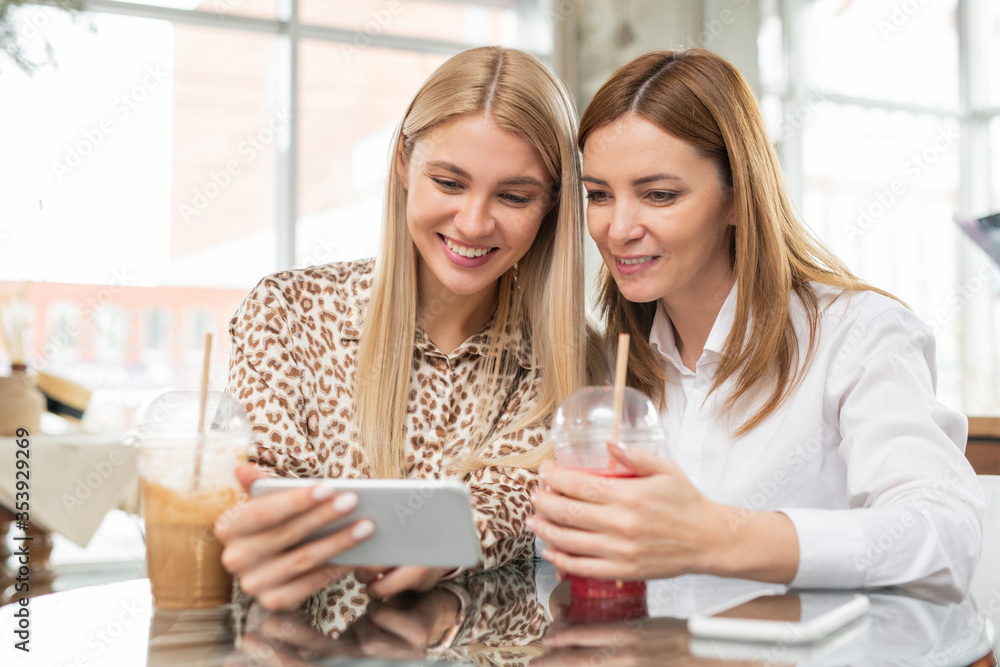 Φωτογραφία Young blond female showing new photos in smartphone to her mother in cafe