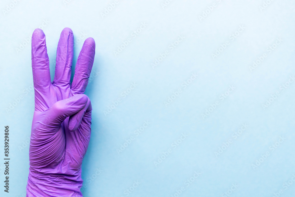 Hand of surgeon in violet medical glove showing three fingers gesture, isolated on a light blue background. Hand of surgeon in violet medical glove showing three fingers gesture, isolated on a light blue background.