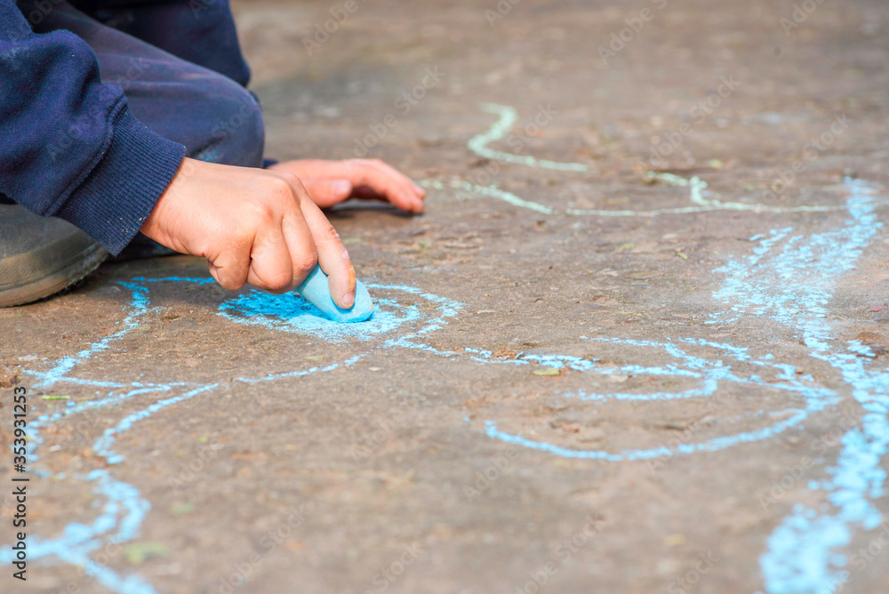 The child drawing a chalk on asphalt. Child drawings paintings on asphalt concept. Kid is playing with colored chalks The child drawing a chalk on asphalt. Child drawings paintings on asphalt concept. Kid is playing with colored chalks