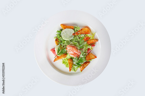 Warm salad of red fish and slices of French fries with vegetables on a white plate. An isolated object.Top view.