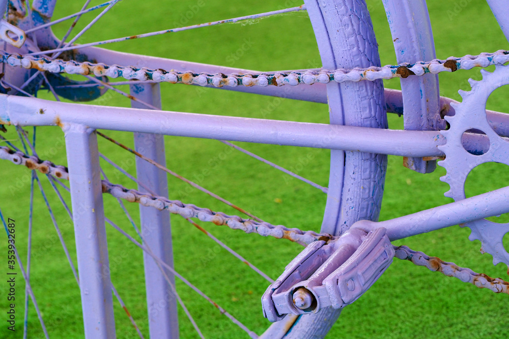 Fragment of a vintage purple bicycle on a green grass background. Bike pedal and part of the rear wheel