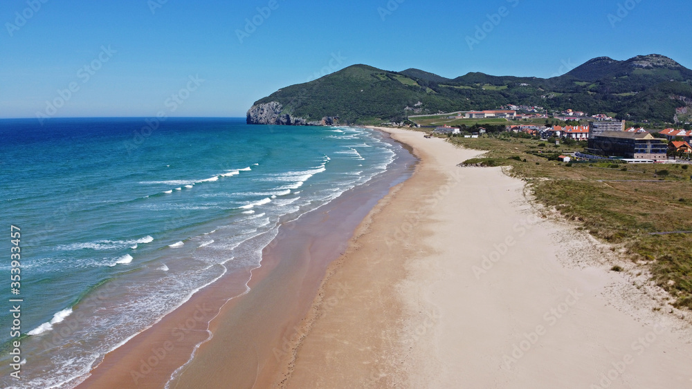 Vista aérea lateral de la playa de Berria en Santoña, playa larga con una montaña verde al final, un día de verano
