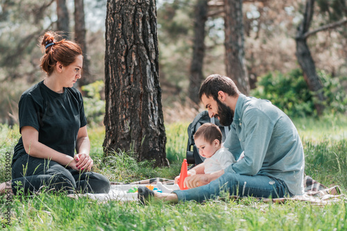 Happy young family with small 8 month daughter having picnic in forest. Cute, Happy, Funny family concept. Father and Mother are playing with daughter and smiling.