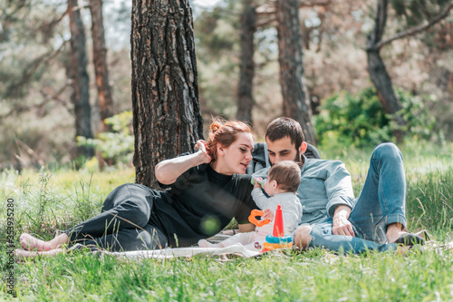Happy young family with small 8 month daughter having picnic in forest. Cute, Happy, Funny family concept. Father and Mother are playing with daughter and smiling.