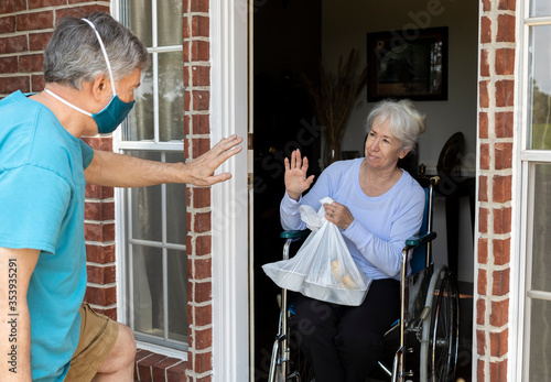 A church volunteer wearing a mask brings food to an elderly woman in a wheelchair that may otherwise be unable to get groceries during COVID19. © JHDT Productions