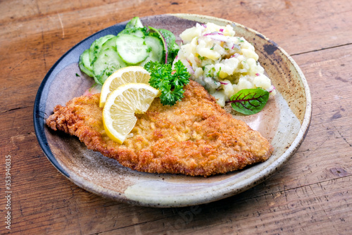 Traditional deep fried veal steak with potato and cucumber salad offered as closeup on a rustic plate with copy space