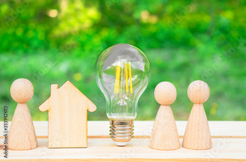 Family concept. Wooden house, lightbulb and many little men on a wooden table. Energy saving, debts for utility bills. Copy space photo