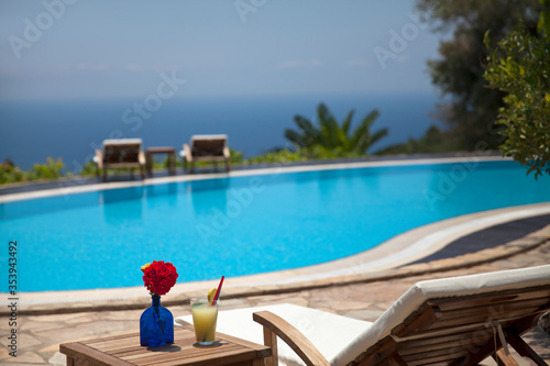 Summer and vacation concept. A glass of cocktail and colorful flowers. Sunbed, swimming pool and a wonderful sea view