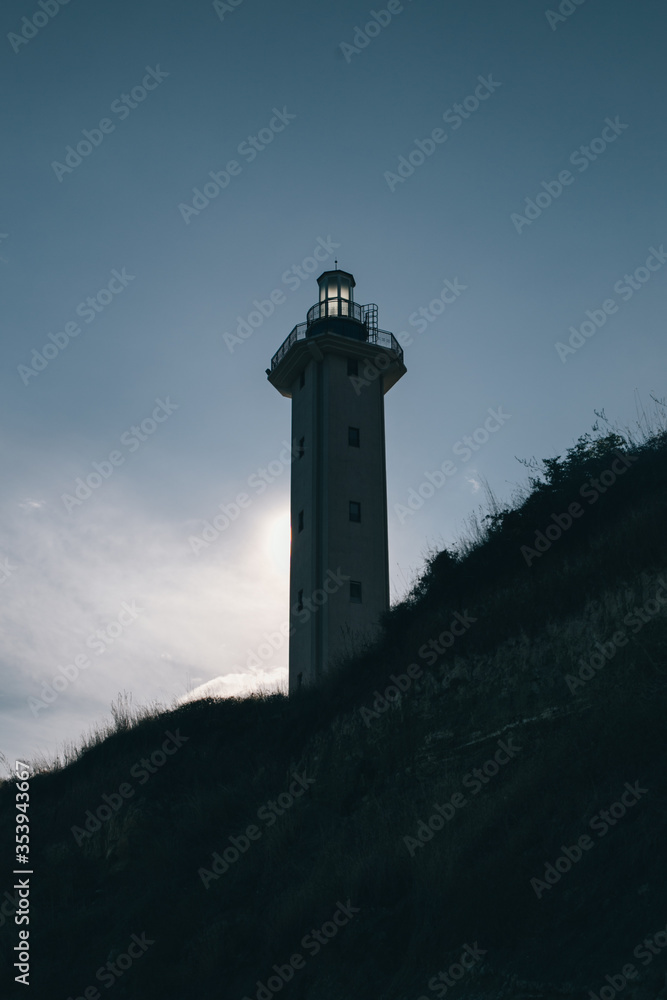 bottom view of a lighthouse on a coast hiding the sun