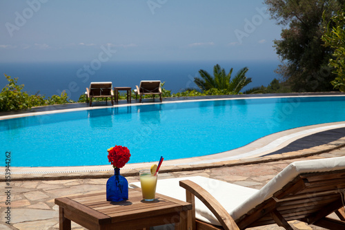 Fresh summer cocktail and sunbed. Swimming pool with mediterranean background.