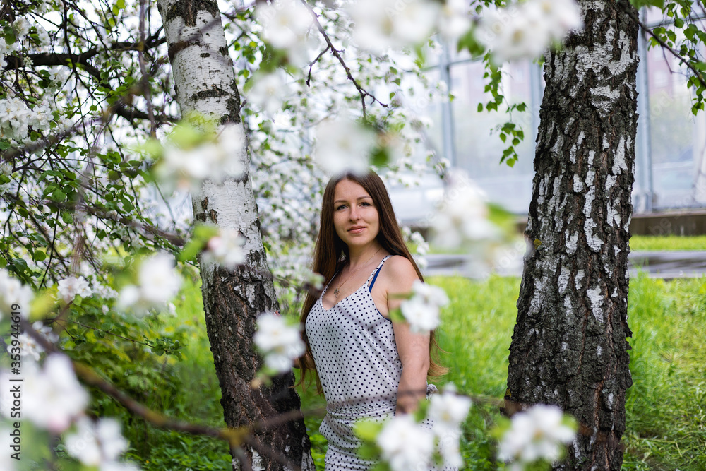 A pretty girl poses in the garden near a blooming Apple tree with white flowers. Spring garden. Beautiful women's hair. Portrait of a beautiful model. A pretty girl poses in the garden near a blooming Apple tree with white flowers. Spring garden. Beautiful women's hair. Portrait of a beautiful model.