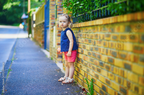 Adorable toddler girl standing against brick wall