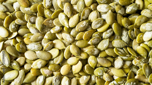 Scattered peeled pumpkin seeds as background. Shelled pumpkin seeds texture. Top view pumpkin seeds closeup
