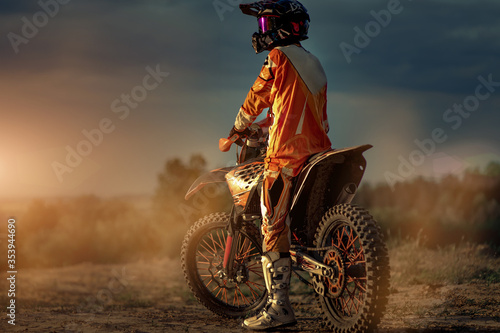 Rear view of a professional motorcyclist preparing before riding in the mountains and then on the off-road. This is a sunset.