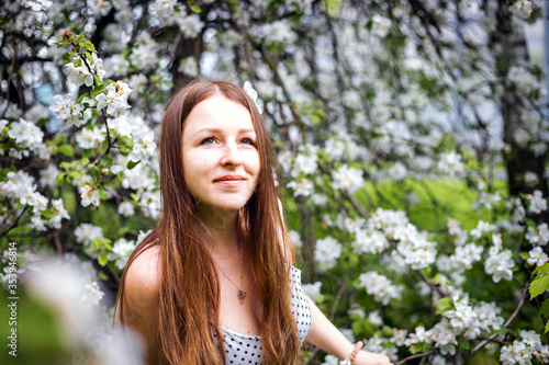Portrait of a beautiful girl with long hair, in an Apple orchard. Spring garden. White flower. An Apple tree blooms in the Park. Model with beautiful hair.