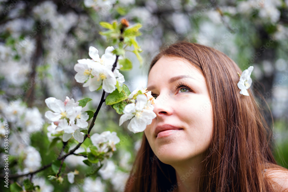 A pretty girl poses in the garden near a blooming Apple tree with white flowers. Spring garden. Beautiful women's hair. Portrait of a beautiful model.