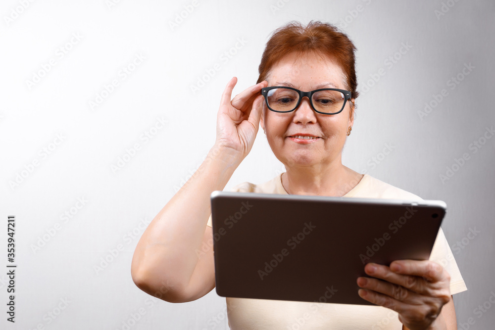 senior woman in glasses with a tablet on a white background in a light T-shirt. place for text, isolated