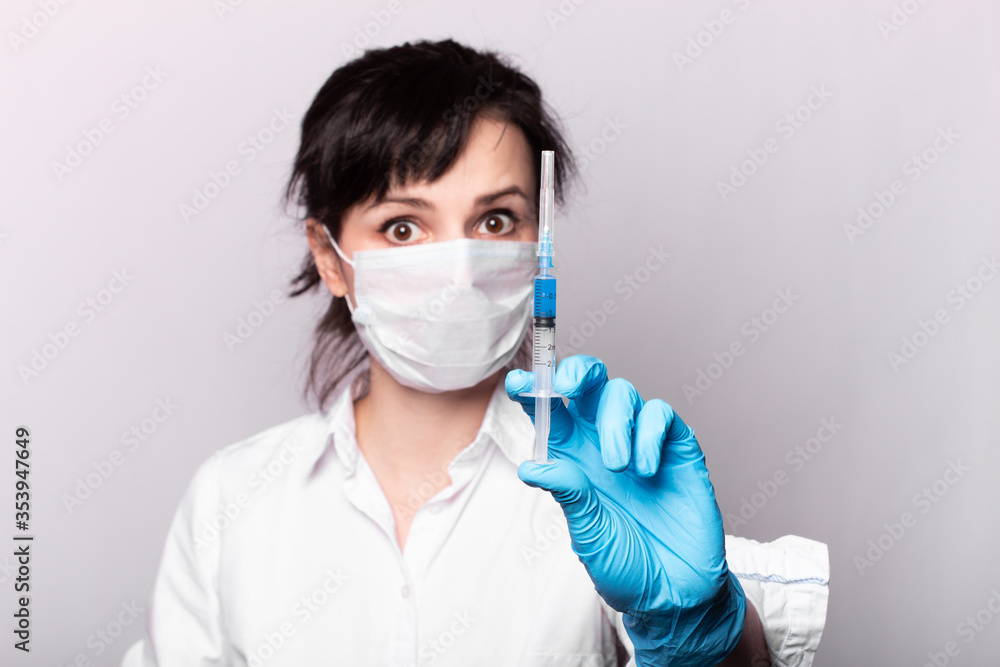 girl in a white shirt, a medical mask and gloves, holds a syringe with blue liquid in her hands