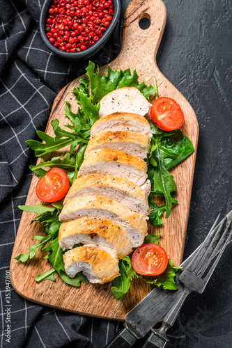Grilled chicken breast. Chicken fillet and fresh vegetable salad with tomatoes and arugula leaves. Black background. Top view
