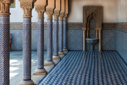 Beautiful oriental architecture. The floor and walls are lined with blue tiles, columns and arches on the left, a drinking water fountain in the corner.