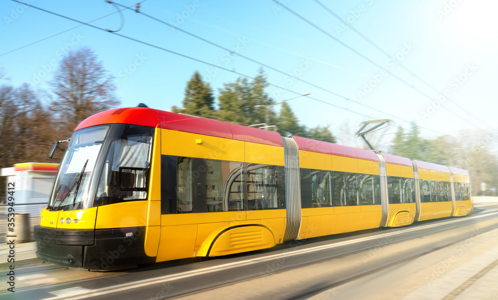 Modern urban rail transport. Yellow tram with motion blur effect moves fast in the city. High speed passenger train in motion on railroad.