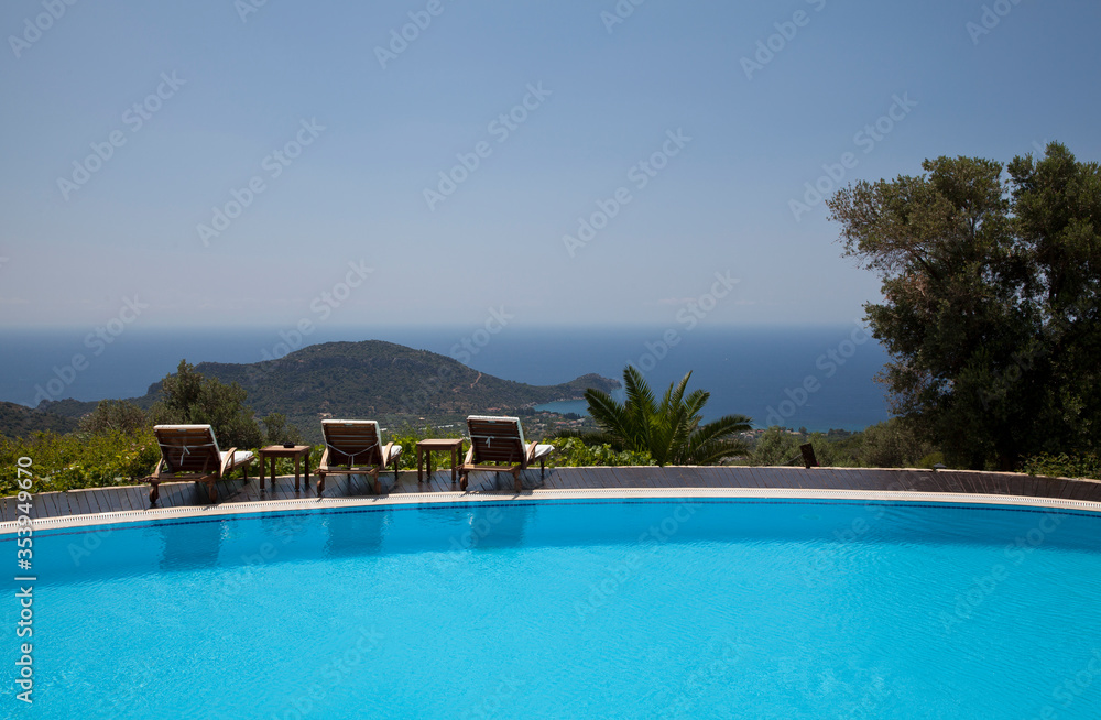 Swimming pool in the garden and beautiful sea and mountain landscape with trees and empty lounge chairs.