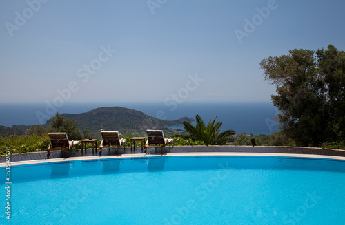 Swimming pool in the garden and beautiful sea and mountain landscape with trees and empty lounge chairs. © Cumhur