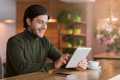 Joyful businessman reading news on digital tablet at cafe