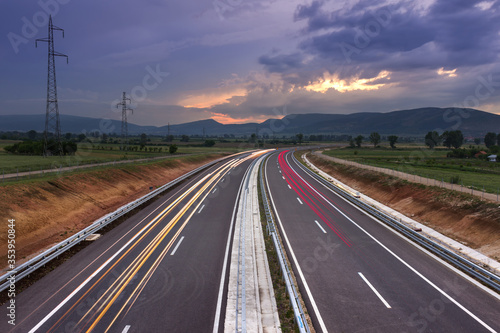 Highway, lines and car-trails leading in to dramatic sunset with colorful, fluffy clouds
