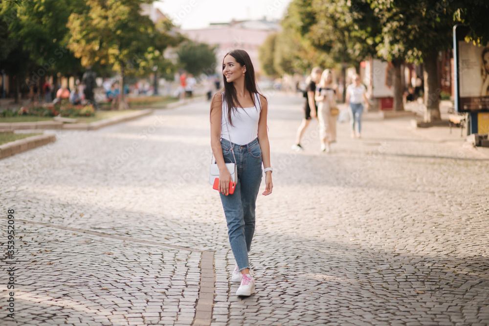 Fototapeta premium Attractive young woman walking by herself in centre of city in summer time. Woman walk alone. Happy woman outdoors. Social distancing