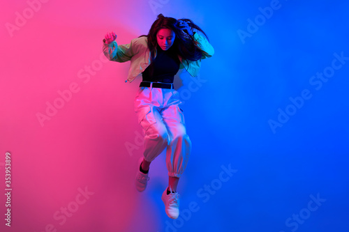 The brunette dances in neon, the dancer in red-blue. Hip hop girl, party, smile. Model in flight, jumping.