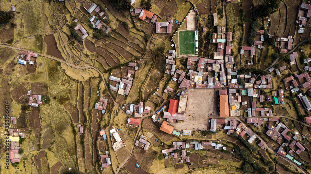 Fototapeta premium Aerial top-down view of main square at Taquile Island, visible houses, football field, terraced slopes, agriculture fields. Lake Titicaca, Peru.