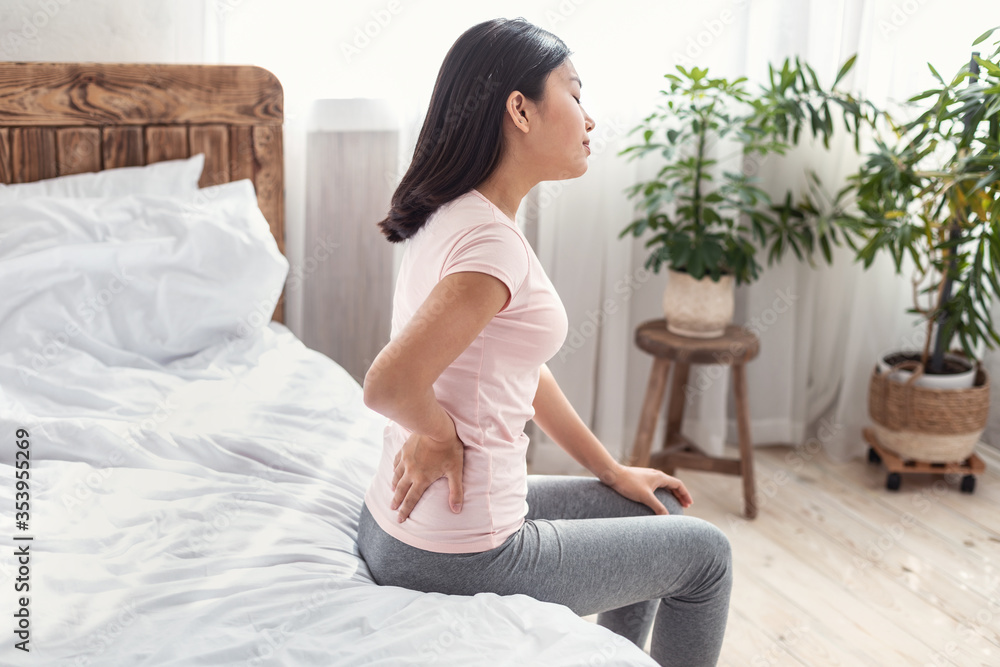 Asian Lady Suffering From Pain In Back Sitting On Bed Asian Lady Suffering From Pain In Back Sitting On Bed