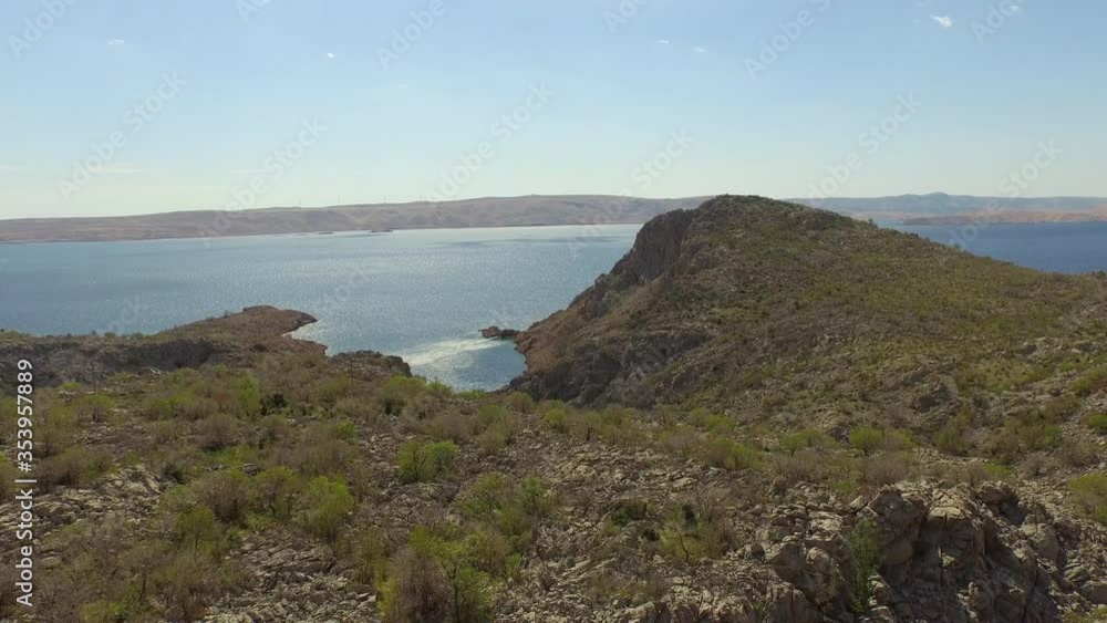 Aerial shot of rocky mountains near sea against sky, drone flying backward over natural landscape on sunny day - Pag, Croatia Aerial shot of rocky mountains near sea against sky, drone flying backward over natural landscape on sunny day - Pag, Croatia